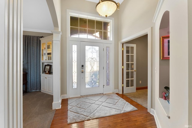 entrance foyer with wood-type flooring, a towering ceiling, and ornamental molding