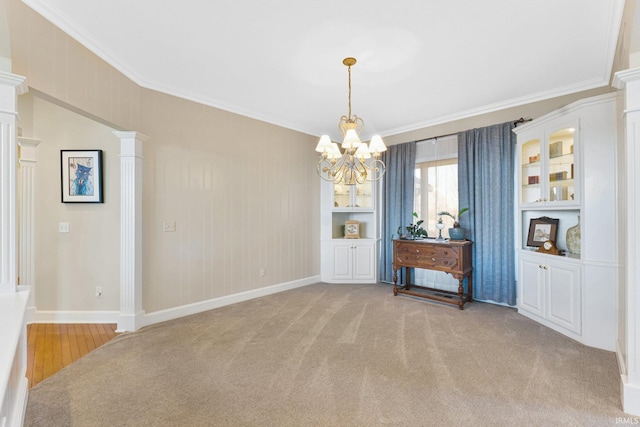 unfurnished dining area with ornamental molding, light colored carpet, a chandelier, and ornate columns