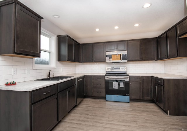 kitchen with dark brown cabinetry, sink, light wood-type flooring, stainless steel appliances, and backsplash