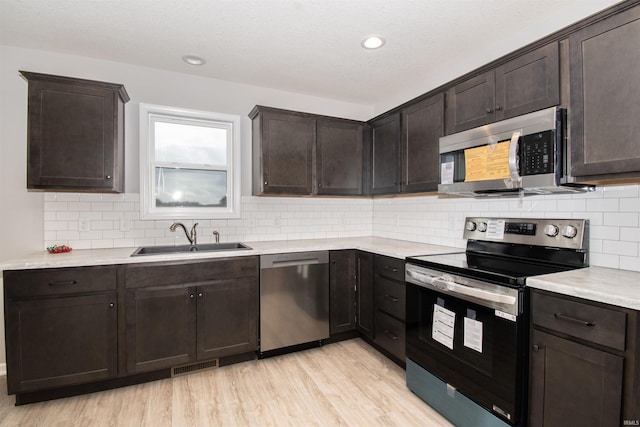 kitchen with sink, appliances with stainless steel finishes, dark brown cabinetry, tasteful backsplash, and light wood-type flooring