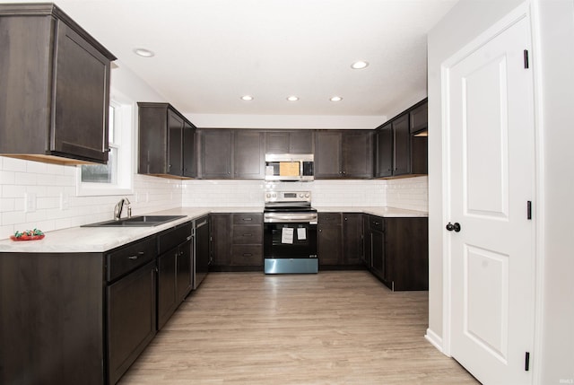 kitchen with appliances with stainless steel finishes, sink, dark brown cabinets, and light hardwood / wood-style flooring