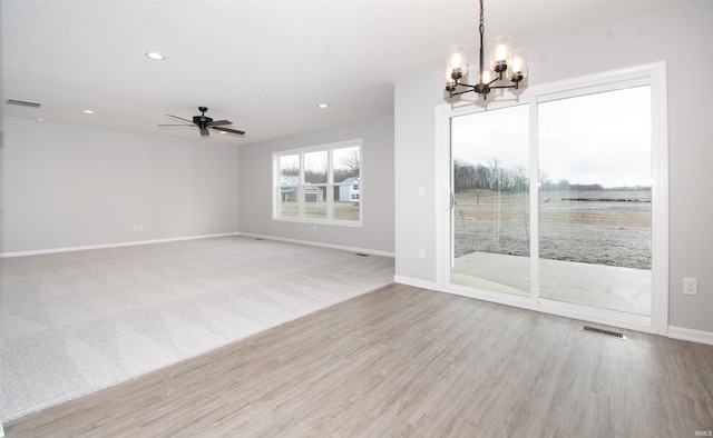 empty room with ceiling fan with notable chandelier and light wood-type flooring