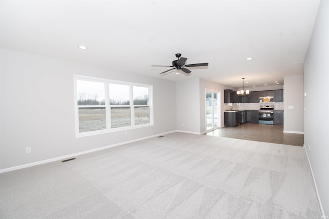 unfurnished living room with carpet, plenty of natural light, and ceiling fan with notable chandelier