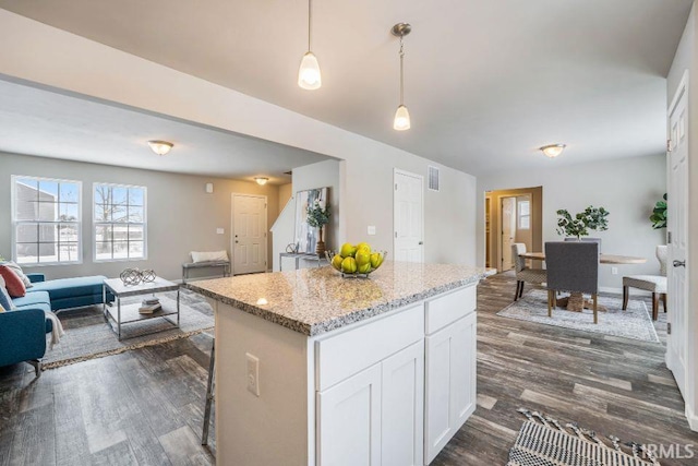 kitchen with white cabinetry, decorative light fixtures, dark hardwood / wood-style flooring, a kitchen island, and light stone countertops