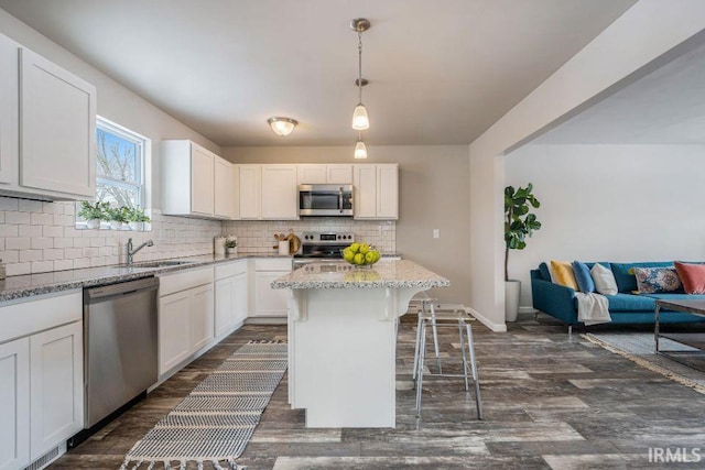 kitchen with light stone counters, a kitchen island, pendant lighting, stainless steel appliances, and white cabinets