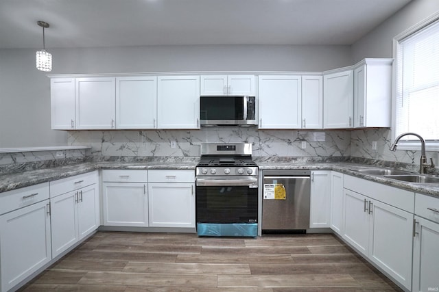 kitchen with appliances with stainless steel finishes, decorative light fixtures, sink, white cabinets, and hardwood / wood-style flooring