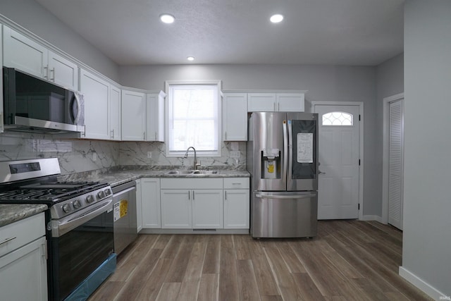 kitchen featuring sink, white cabinetry, stainless steel appliances, light stone counters, and wood-type flooring