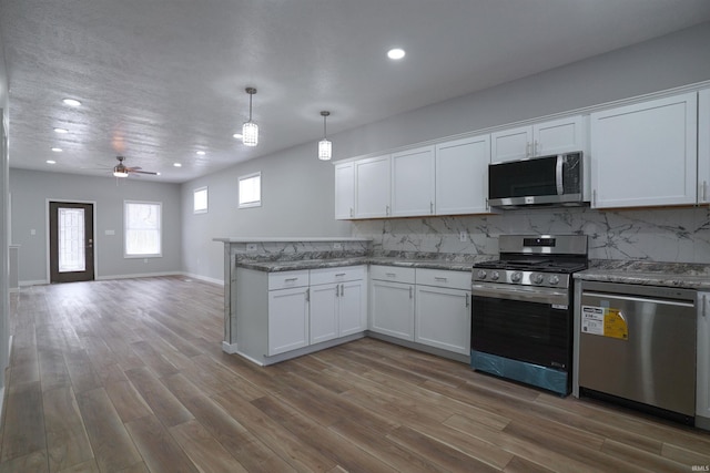 kitchen with pendant lighting, hardwood / wood-style flooring, white cabinetry, stainless steel appliances, and tasteful backsplash