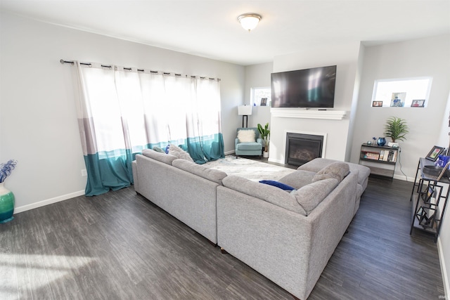 living area with dark wood-style floors, a glass covered fireplace, and baseboards