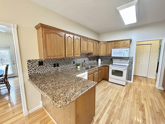 kitchen with sink, kitchen peninsula, white appliances, and dark stone counters