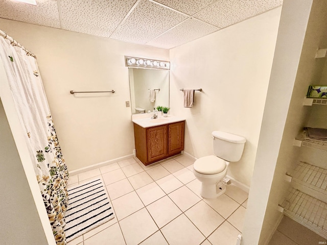 bathroom featuring tile patterned flooring, vanity, a drop ceiling, and toilet