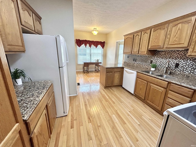 kitchen featuring sink, white appliances, tasteful backsplash, light hardwood / wood-style floors, and a textured ceiling