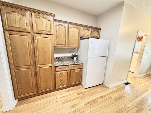 kitchen with white fridge, dark stone countertops, and light hardwood / wood-style flooring