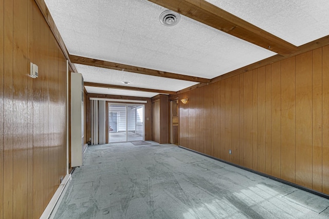 carpeted spare room featuring wooden walls, beam ceiling, and a textured ceiling