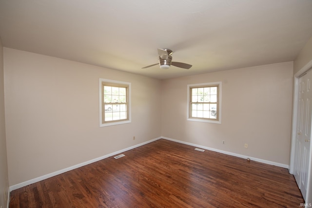 empty room featuring dark wood-type flooring, ceiling fan, and a healthy amount of sunlight