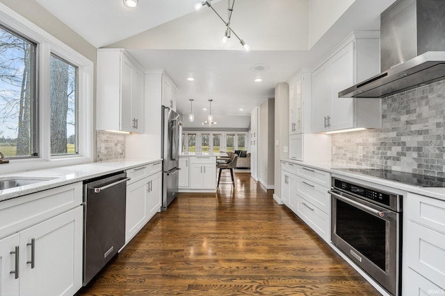 kitchen with wall chimney exhaust hood, white cabinetry, decorative light fixtures, appliances with stainless steel finishes, and dark hardwood / wood-style flooring