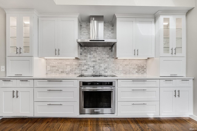 kitchen featuring dark wood-type flooring, wall chimney exhaust hood, black electric stovetop, oven, and white cabinets