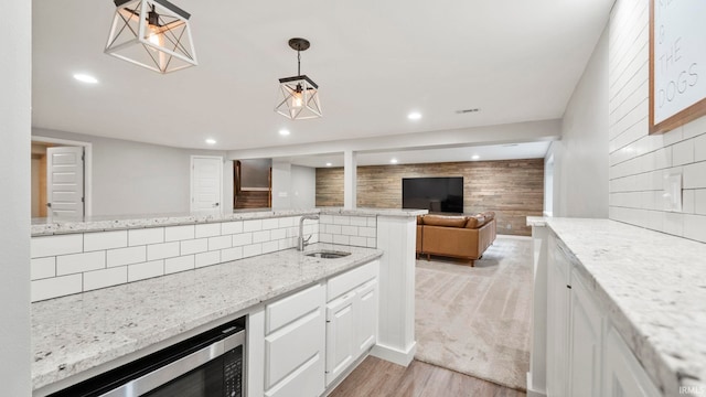 kitchen featuring sink, white cabinetry, stainless steel microwave, pendant lighting, and light stone countertops