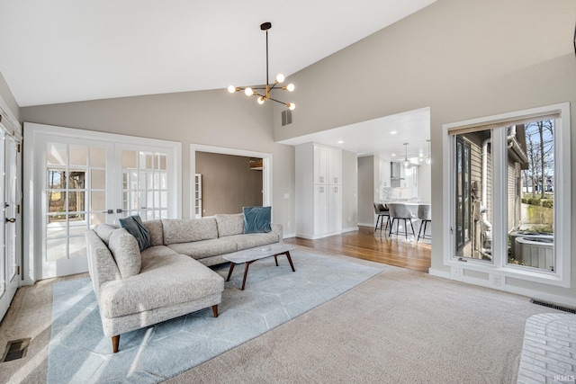 carpeted living room with an inviting chandelier, high vaulted ceiling, and french doors