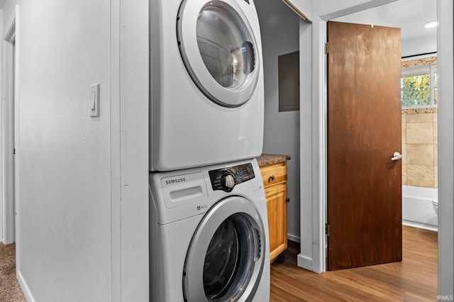 washroom with stacked washer / drying machine, light hardwood / wood-style floors, and cabinets