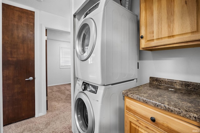 laundry room with stacked washer and dryer, light colored carpet, and cabinets