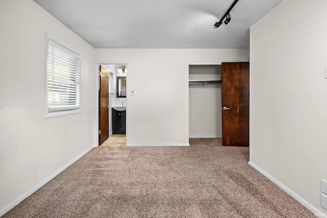 unfurnished bedroom with light colored carpet, ensuite bathroom, track lighting, and a closet