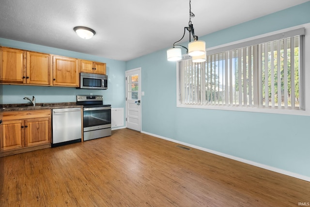 kitchen with stainless steel appliances, decorative light fixtures, light hardwood / wood-style floors, and sink