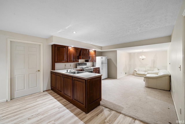 kitchen featuring sink, an inviting chandelier, stainless steel range oven, kitchen peninsula, and white fridge