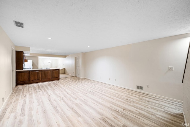 unfurnished living room with a textured ceiling and light hardwood / wood-style floors