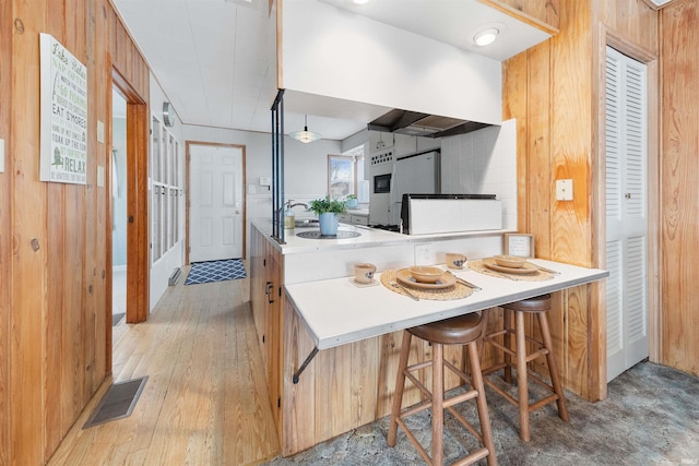 kitchen with kitchen peninsula, light wood-type flooring, a breakfast bar area, and wood walls