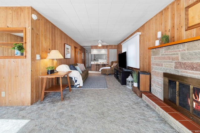 carpeted living room featuring ceiling fan, a stone fireplace, and wood walls