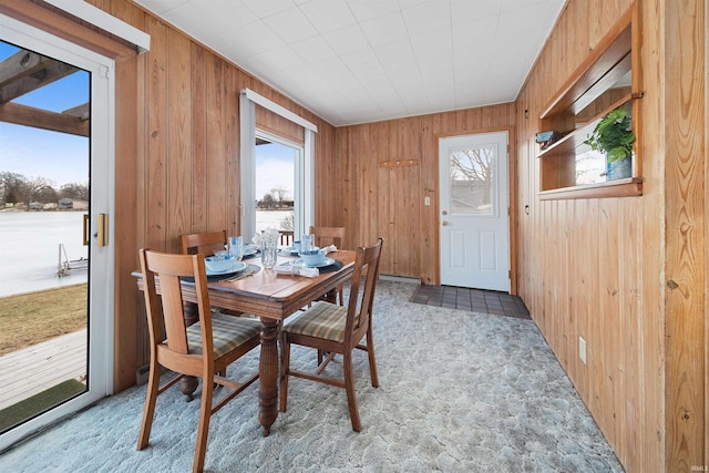 carpeted dining space featuring wood walls