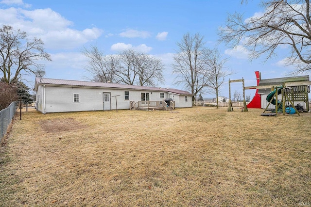 rear view of house featuring a wooden deck, a playground, and a lawn