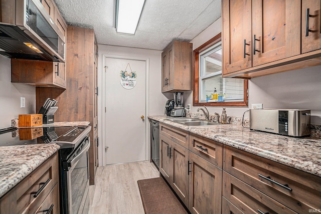 kitchen with sink, light stone counters, a textured ceiling, appliances with stainless steel finishes, and light hardwood / wood-style floors