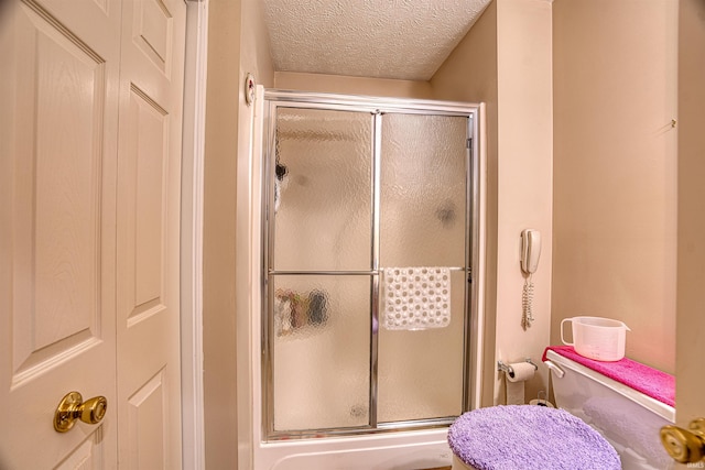 bathroom featuring a shower with door, toilet, and a textured ceiling