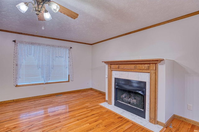 unfurnished living room with ornamental molding, a tiled fireplace, a textured ceiling, and light wood-type flooring