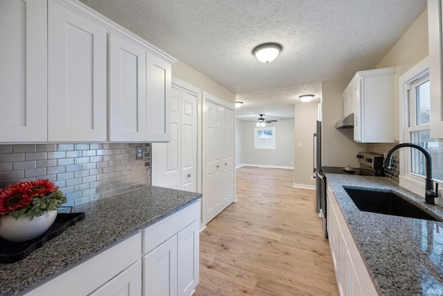 kitchen with white cabinetry, dark stone counters, sink, and light hardwood / wood-style flooring