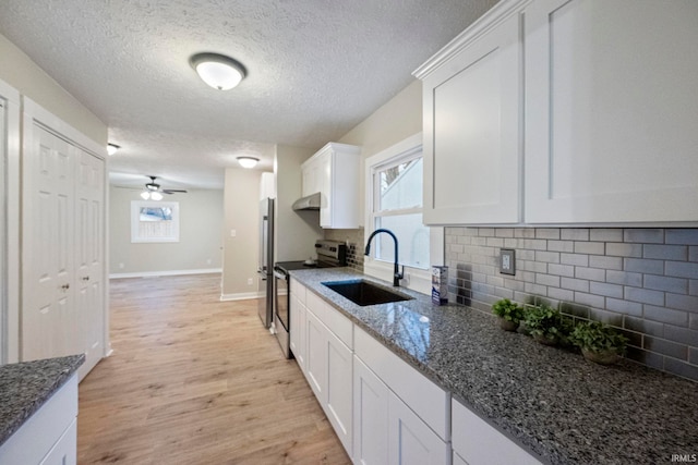 kitchen featuring sink, light hardwood / wood-style flooring, dark stone countertops, stainless steel electric stove, and white cabinets