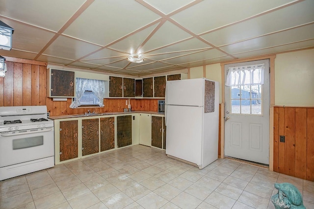 kitchen with sink, white appliances, light tile patterned flooring, and wood walls