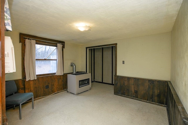 sitting room featuring heating unit, wood walls, a textured ceiling, light carpet, and a wood stove