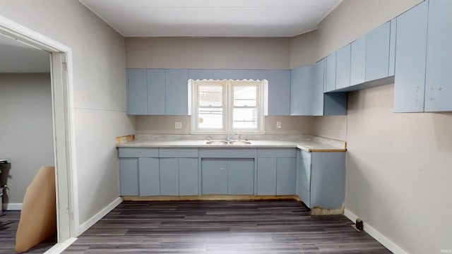 kitchen with dark wood-type flooring, baseboards, a sink, and light countertops