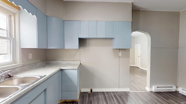 kitchen with light countertops, a baseboard radiator, arched walkways, wood finished floors, and a sink