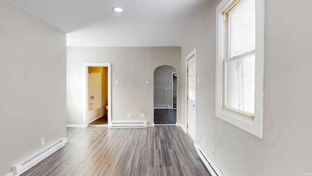 empty room with a baseboard radiator, arched walkways, wood finished floors, and baseboards