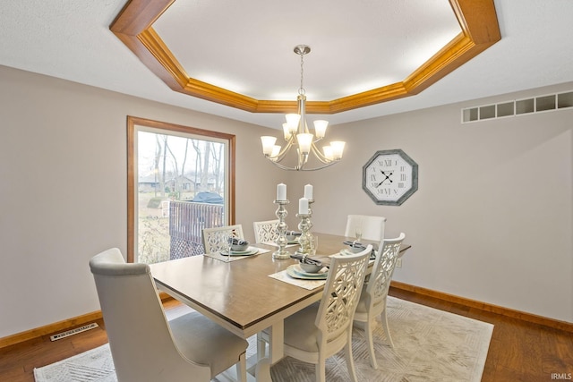 dining room featuring a raised ceiling, ornamental molding, hardwood / wood-style flooring, and a chandelier