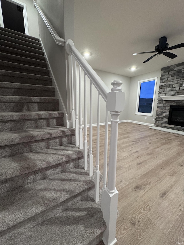 stairway with hardwood / wood-style floors, a fireplace, and ceiling fan