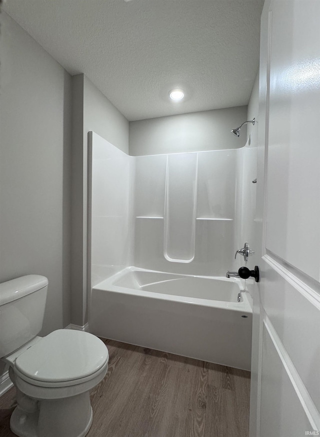 bathroom with hardwood / wood-style floors, a textured ceiling, tub / shower combination, and toilet