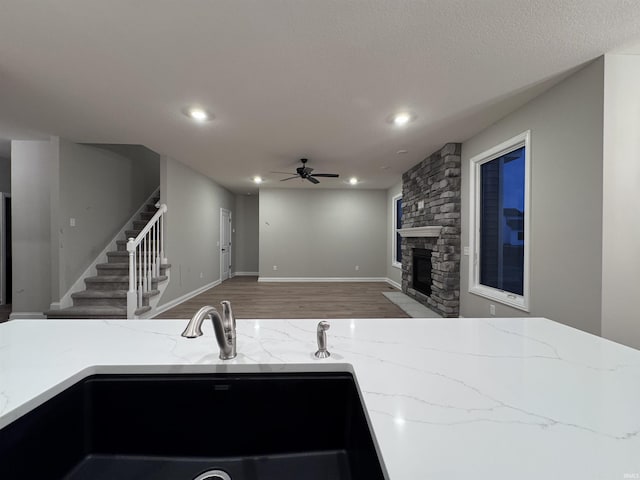 kitchen with a stone fireplace, sink, wood-type flooring, ceiling fan, and light stone countertops