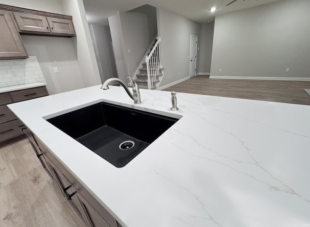 kitchen featuring tasteful backsplash, sink, light hardwood / wood-style floors, and light stone countertops