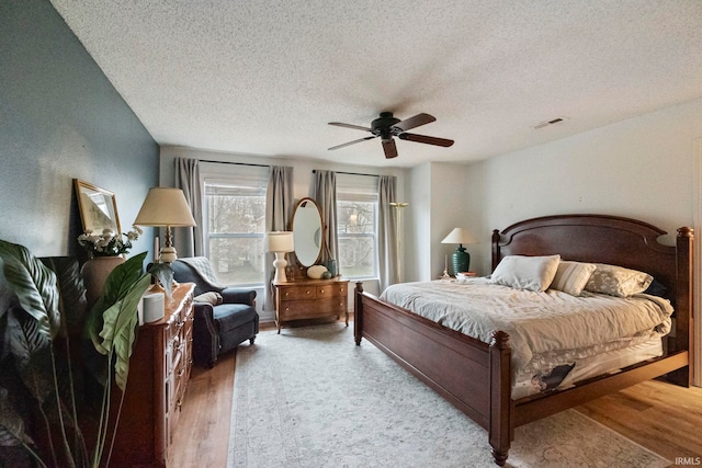 bedroom with ceiling fan, light hardwood / wood-style flooring, and a textured ceiling