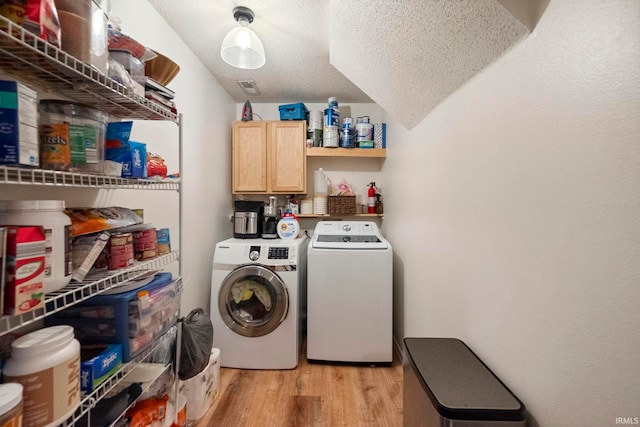 clothes washing area with cabinets, a textured ceiling, independent washer and dryer, and light hardwood / wood-style floors